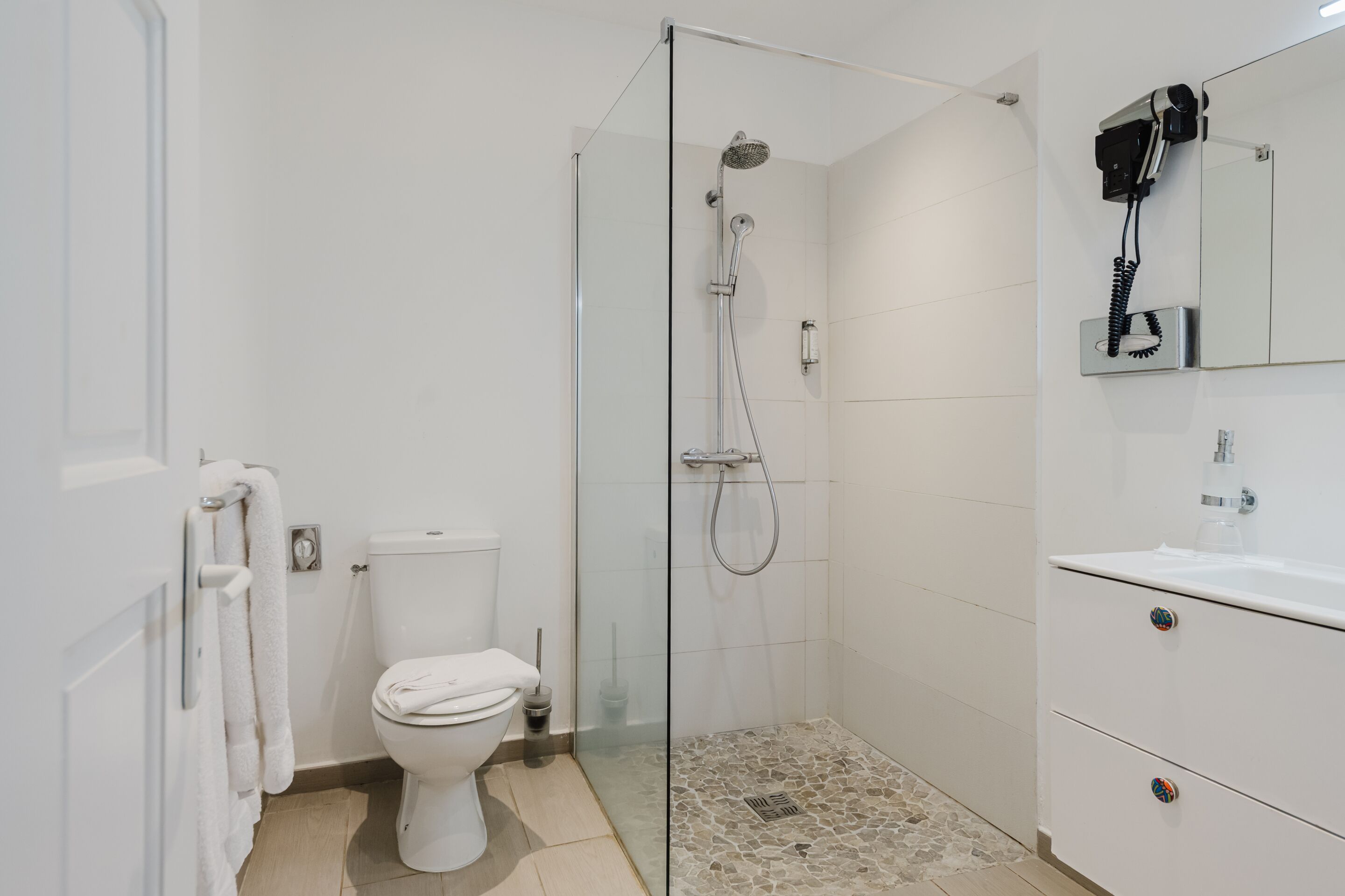 Un bany modern amb dutxa protegida per vidre, un vàter blanc i un lavabo amb mirall i rentaperros.