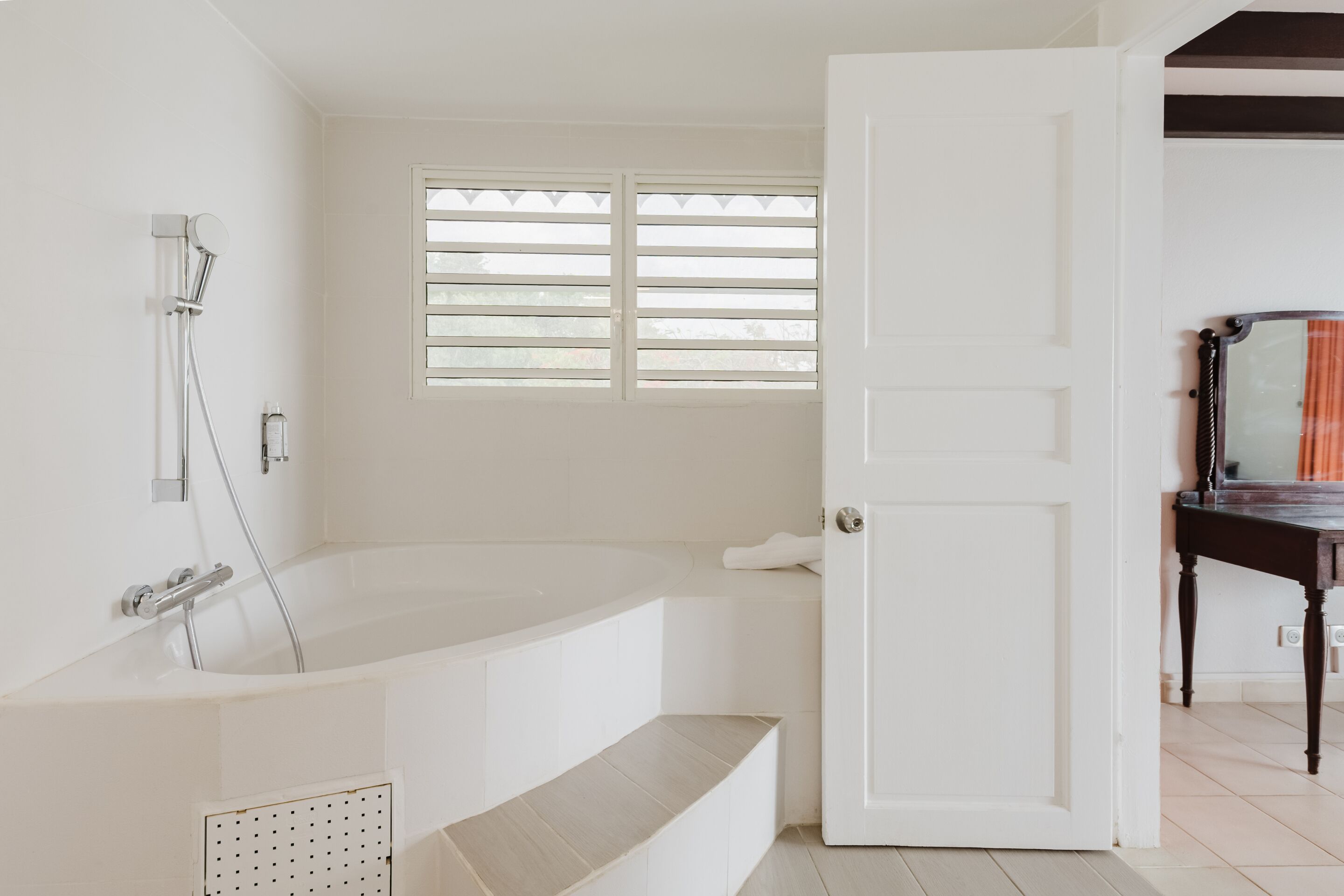 Een badkamer met een witte badkuip, douche en raam met zonwering.