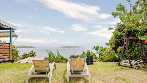 Two wicker lounge chairs facing a view of the sea with a small island in the distance. - Hôtel Frégate Bleue (Le Francois)