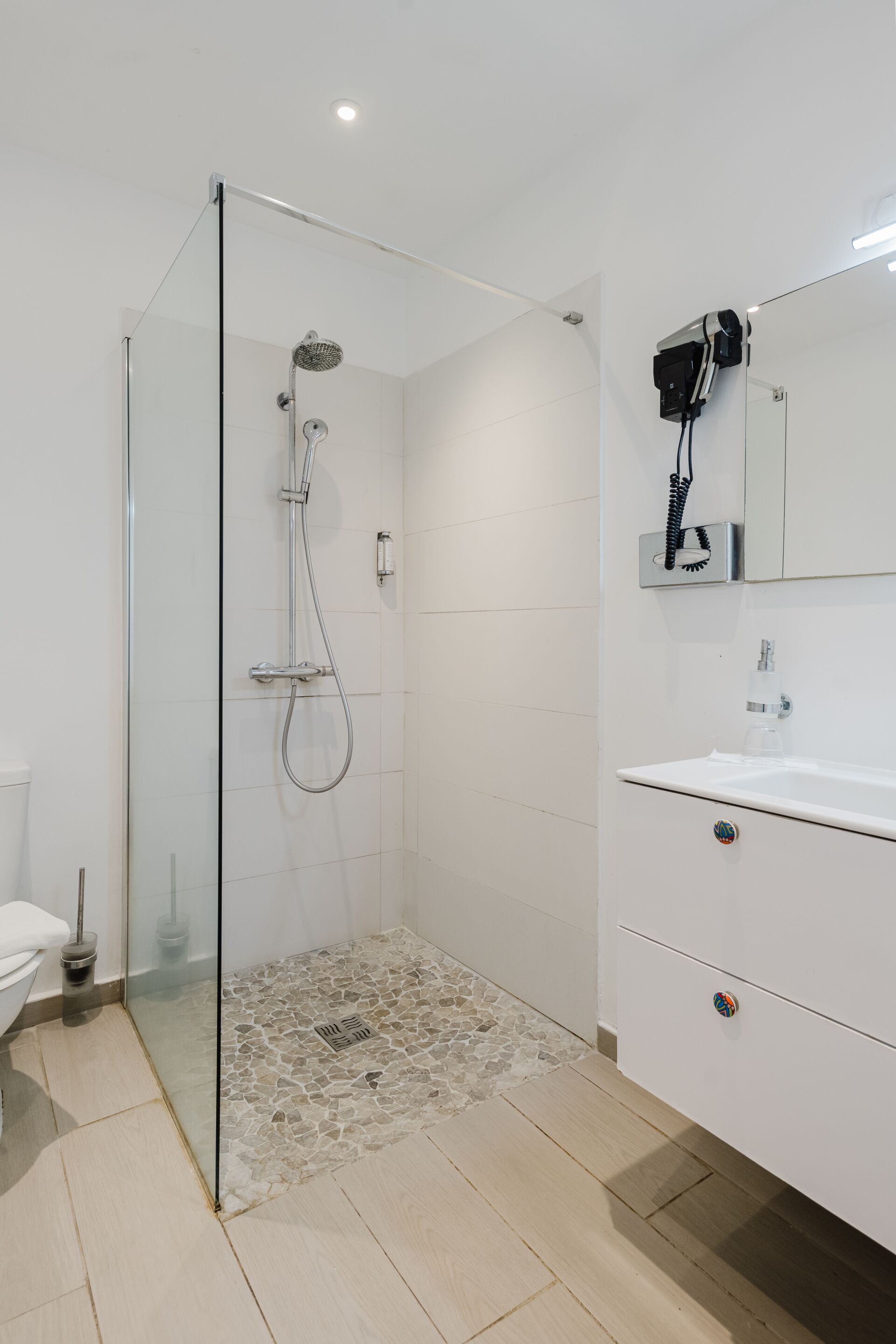 Un baño moderno con ducha de vidrio, lavamanos blanco y espejo con secador de pelo.