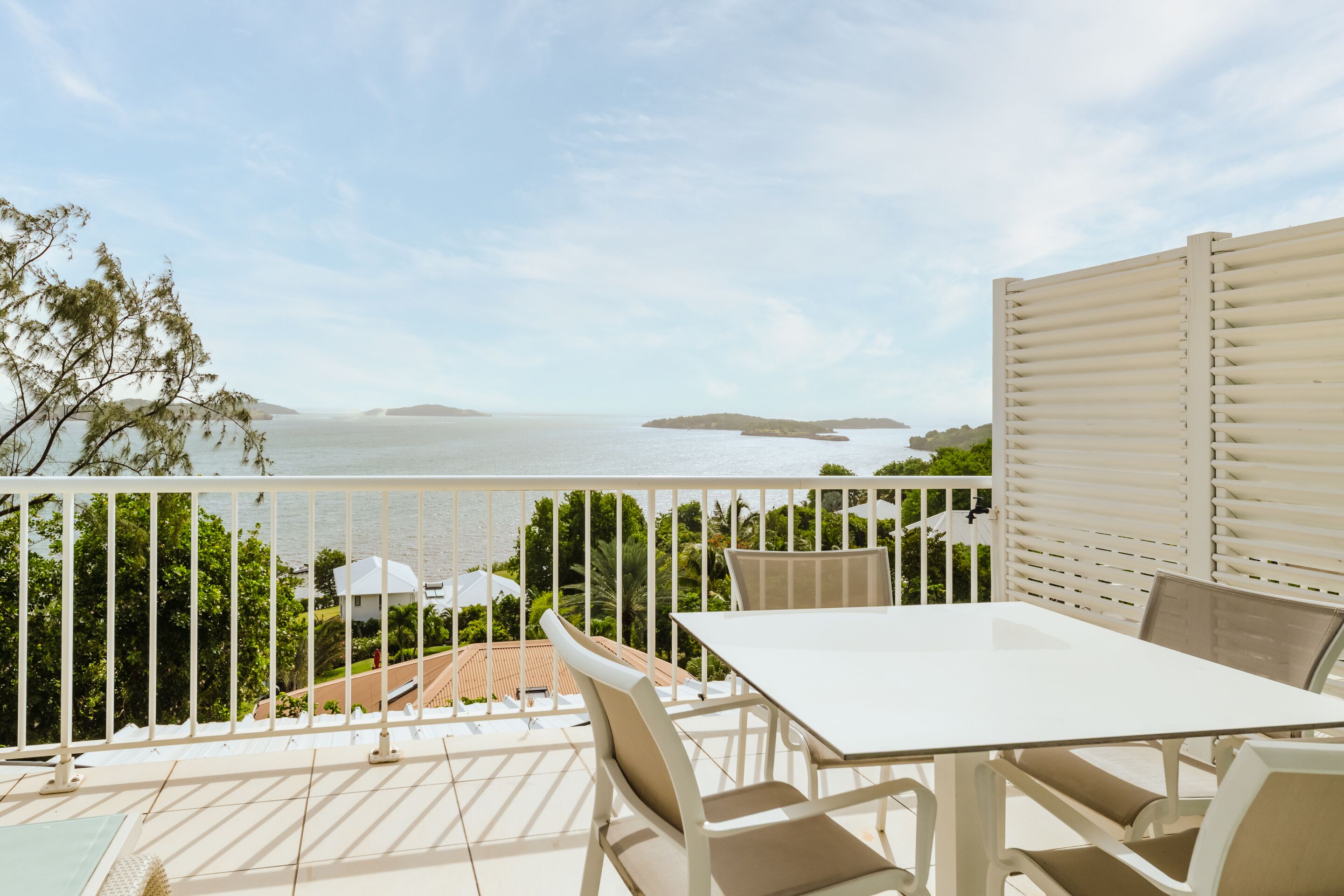 A balcony with a white table and chairs, overlooking a body of water and greenery.