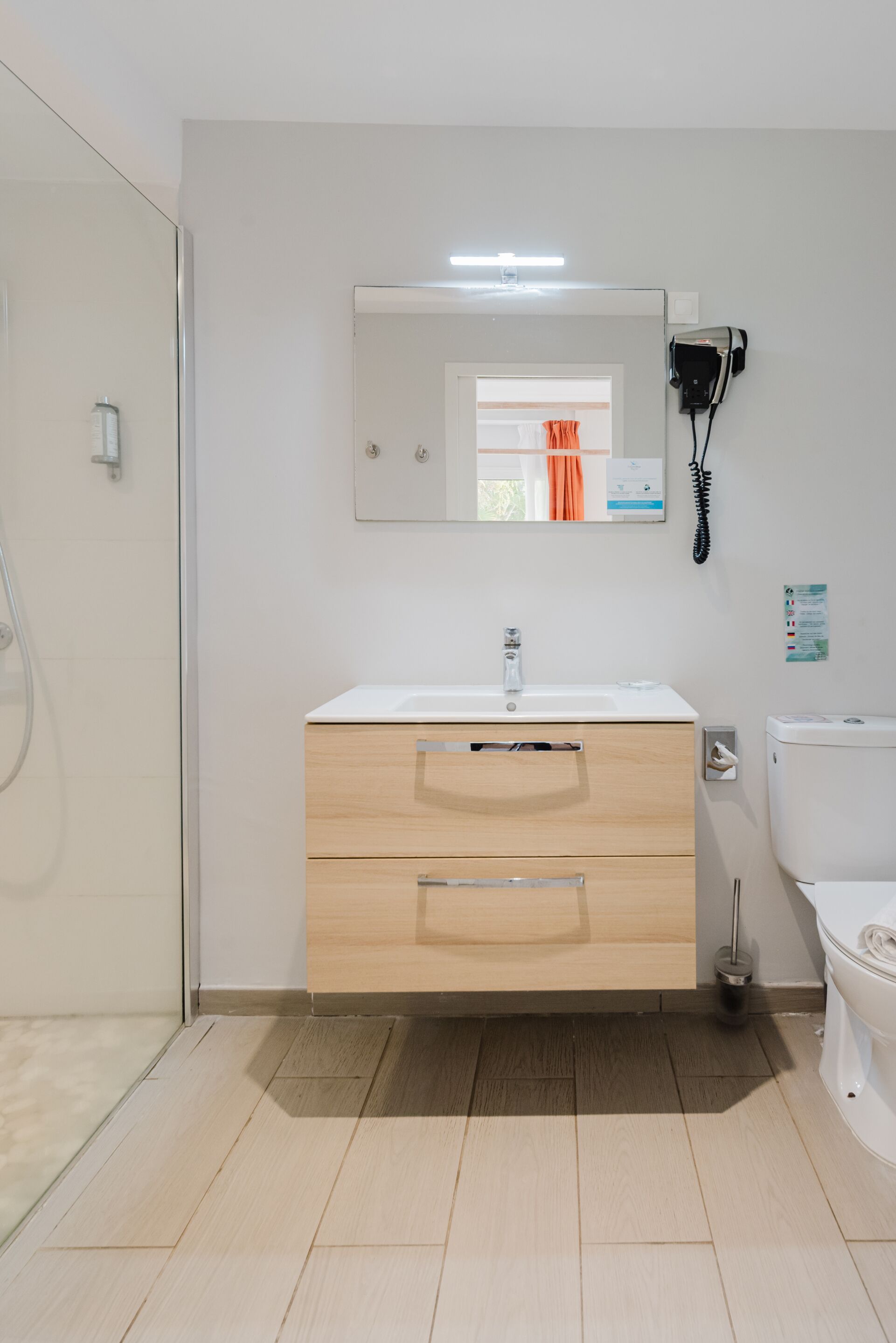 Ein modernes Badezimmer mit Duschkabine aus Glas, einem weißen Waschbecken mit Spiegel darüber und einer Toilette.