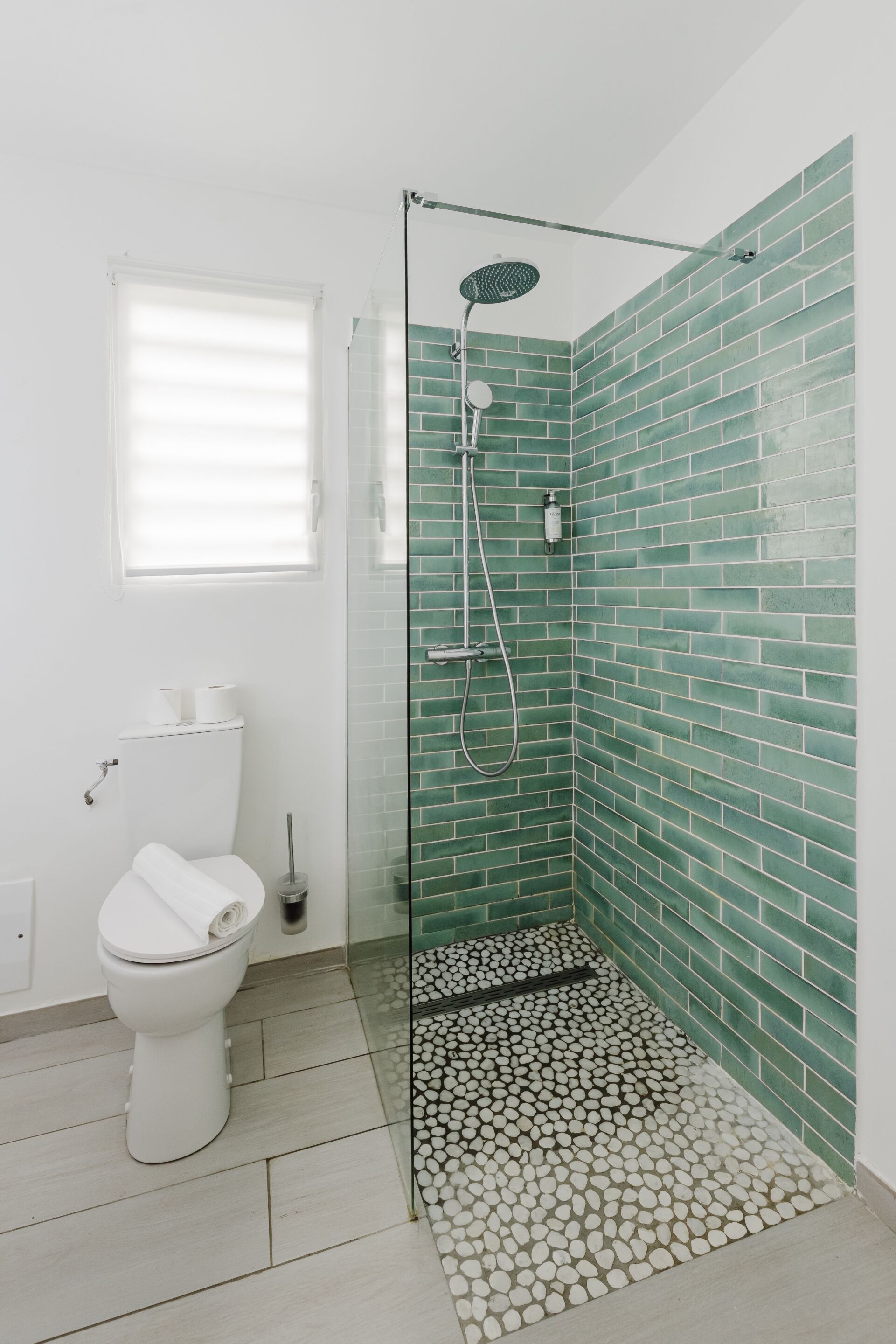 Un baño con ducha de vidrio, inodoro y ventana con persianas.