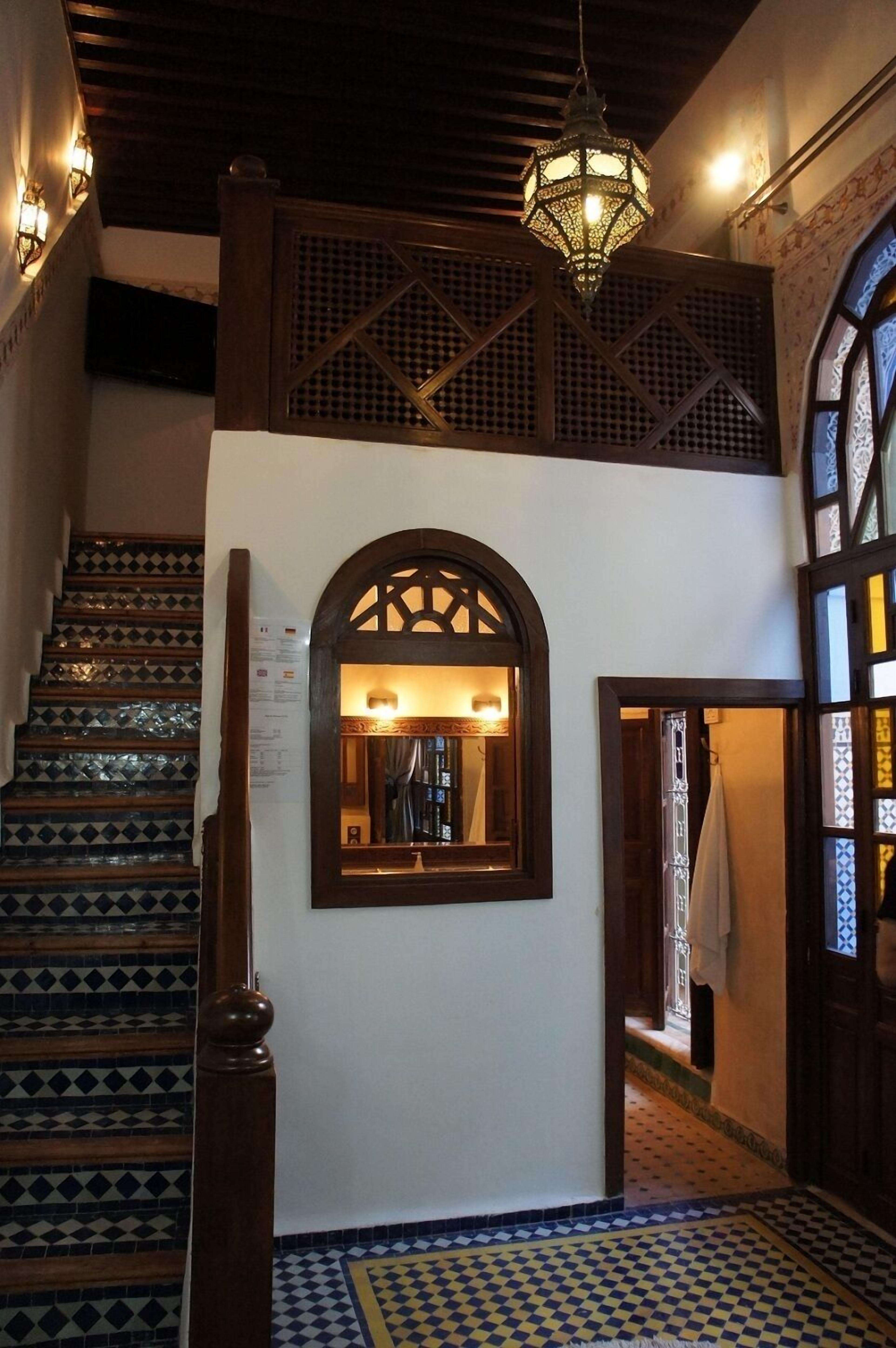 A staircase with patterned tiles, a wooden handrail, and a hanging light fixture.
