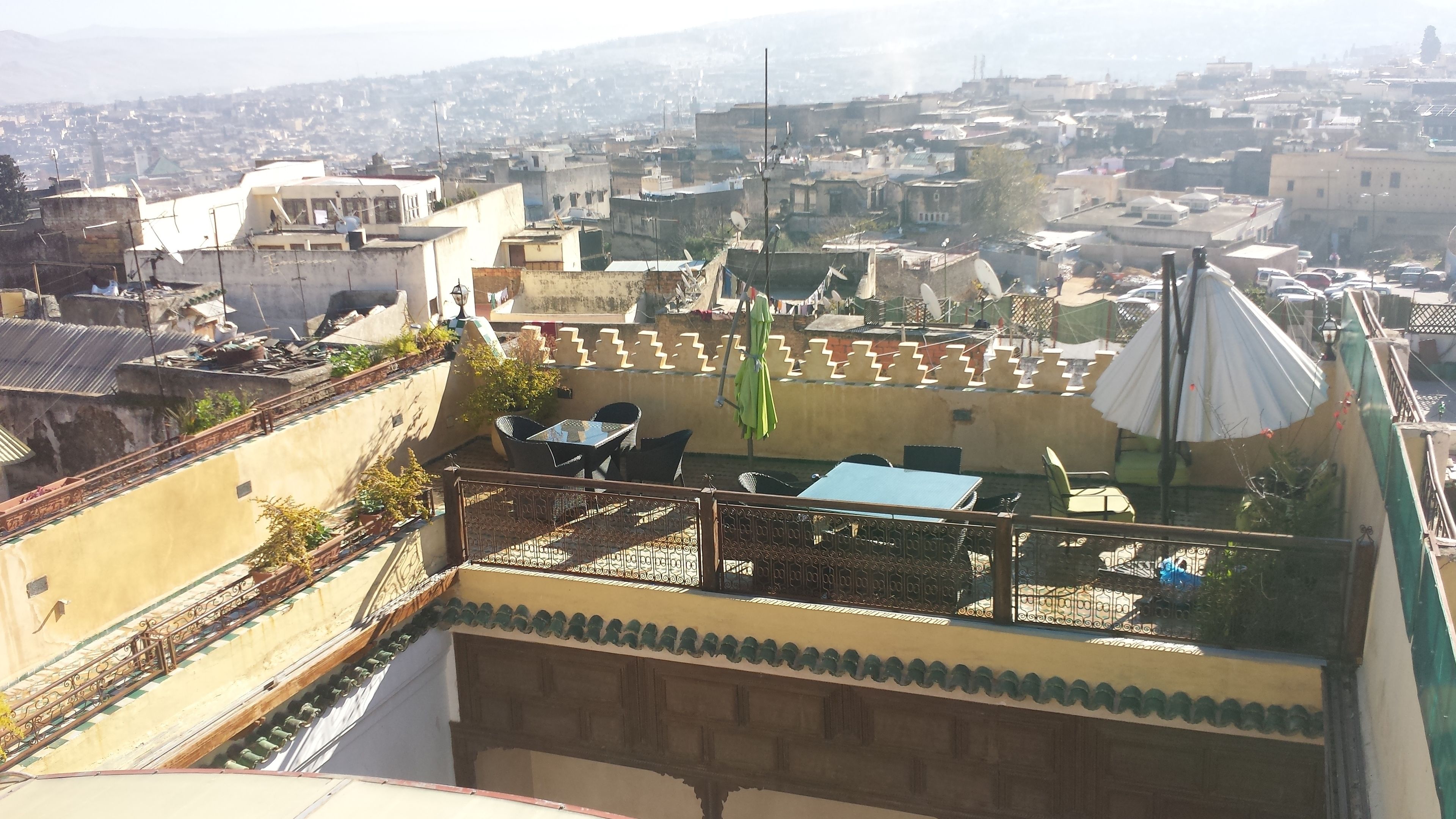 A rooftop terrace with outdoor seating, a view of a densely packed cityscape, and a distant mountain range.