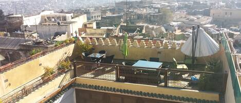 A rooftop terrace with outdoor seating, a view of a densely packed cityscape, and a distant mountain range.