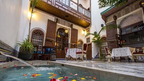 Ein Innenpool mit Seerosen, ein Essbereich mit Tischen und Stühlen sowie traditionelle marokkanische Architektur.