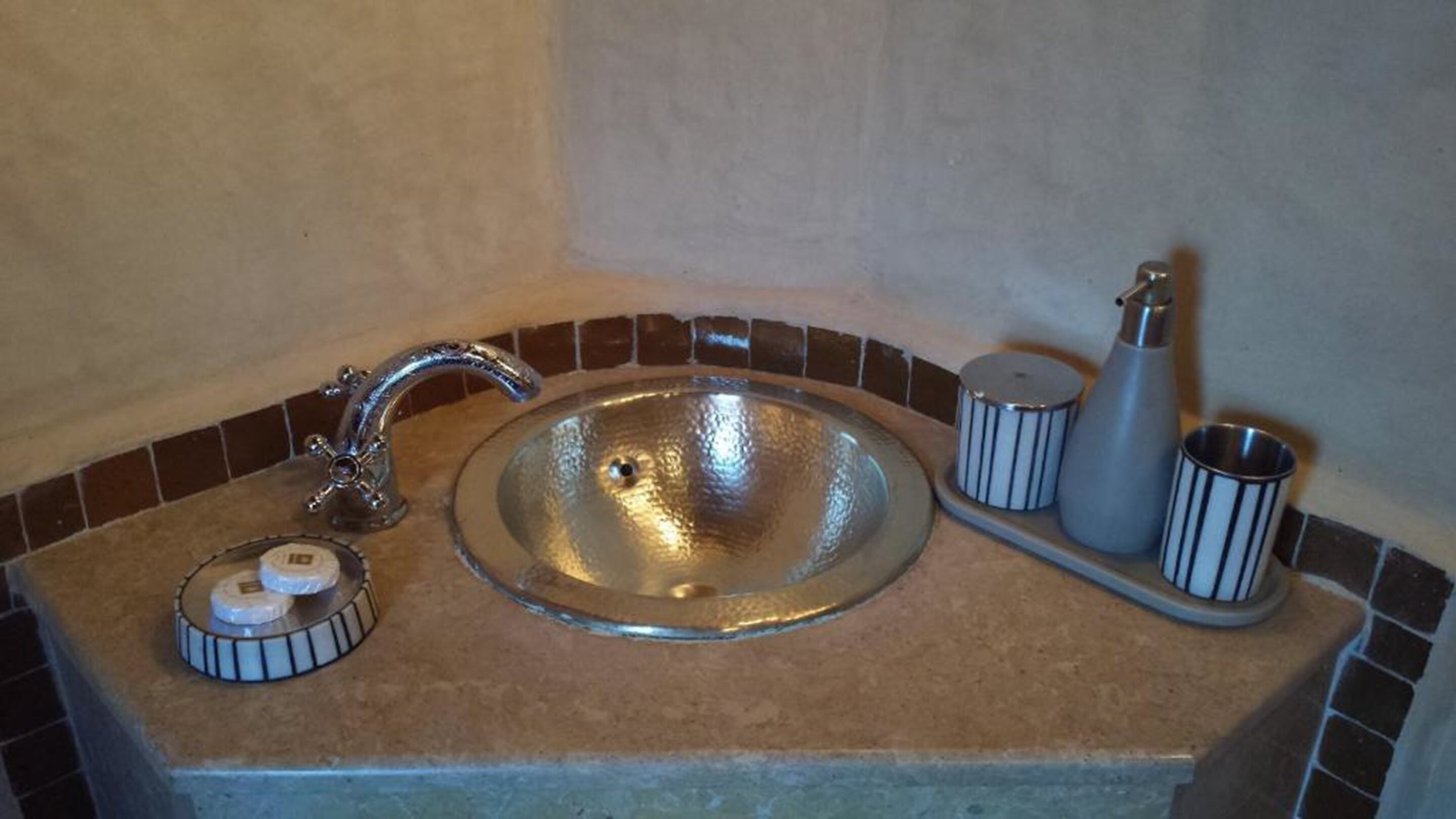A bathroom sink with a chrome faucet, a soap dispenser, and a small container, set against a tiled backsplash.