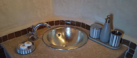 A bathroom sink with a chrome faucet, a soap dispenser, and a small container, set against a tiled backsplash.