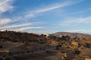 Paisagem costeira com estrada, edifícios e uma colina com ruínas.