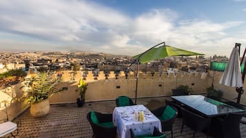 Una terraza con una mesa para dos, una sombrilla verde y vistas a un paisaje urbano.
