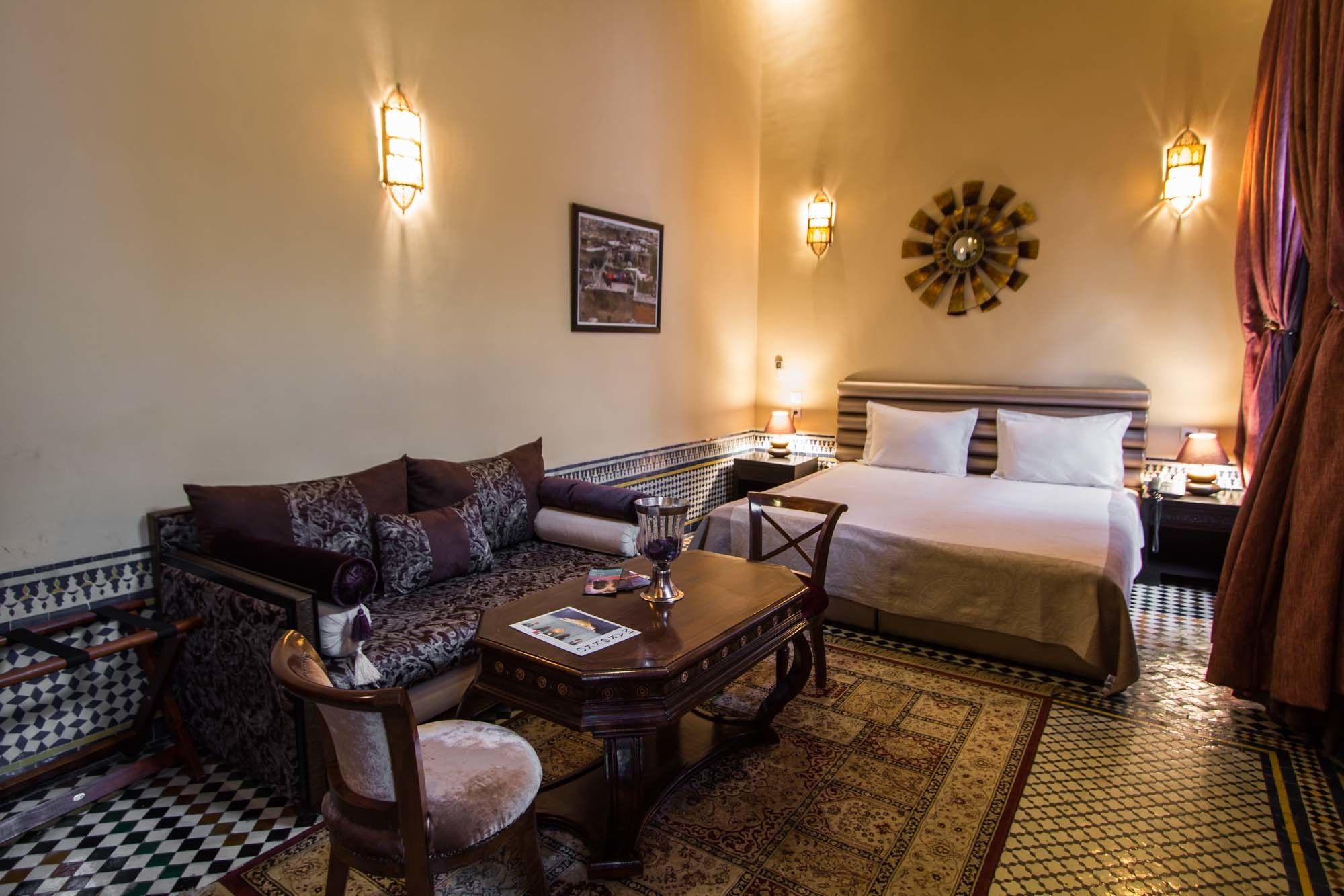 Une chambre d’hôtel équipée d’un canapé, d’une petite table, d’un lit et d’appliques murales décoratives.