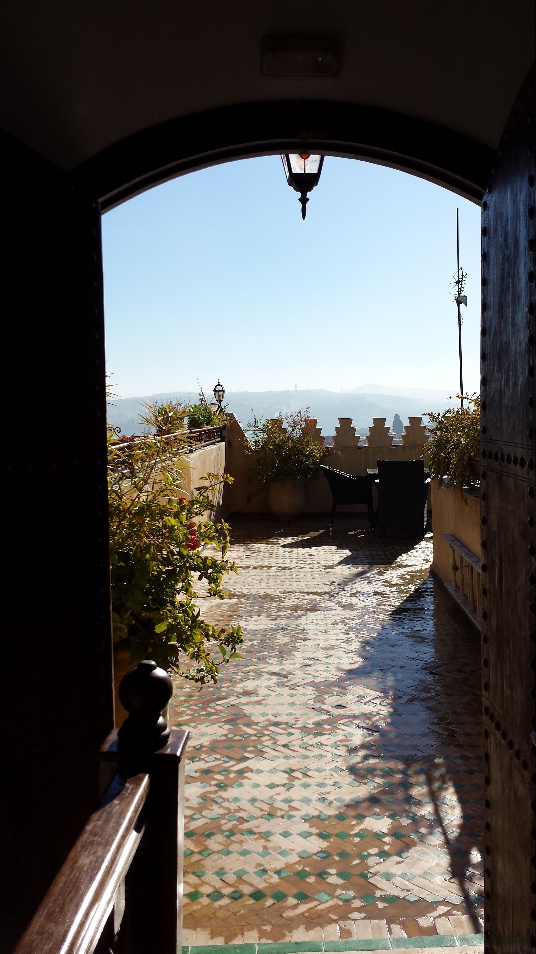 A tiled pathway leading to a terrace with potted plants and a view of the cityscape.