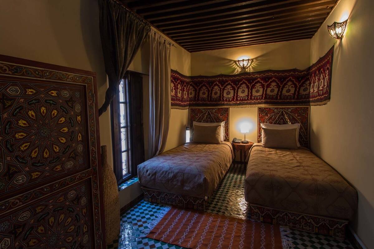 A traditional room with two beds, patterned walls, and a checkered floor.