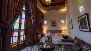 Ein Hotelzimmer mit Schachbrettmuster-Boden, einem Bett mit weißer Bettwäsche, einer Couch, einem kleinen Tisch mit einer Vase und einer Kristallleuchter.