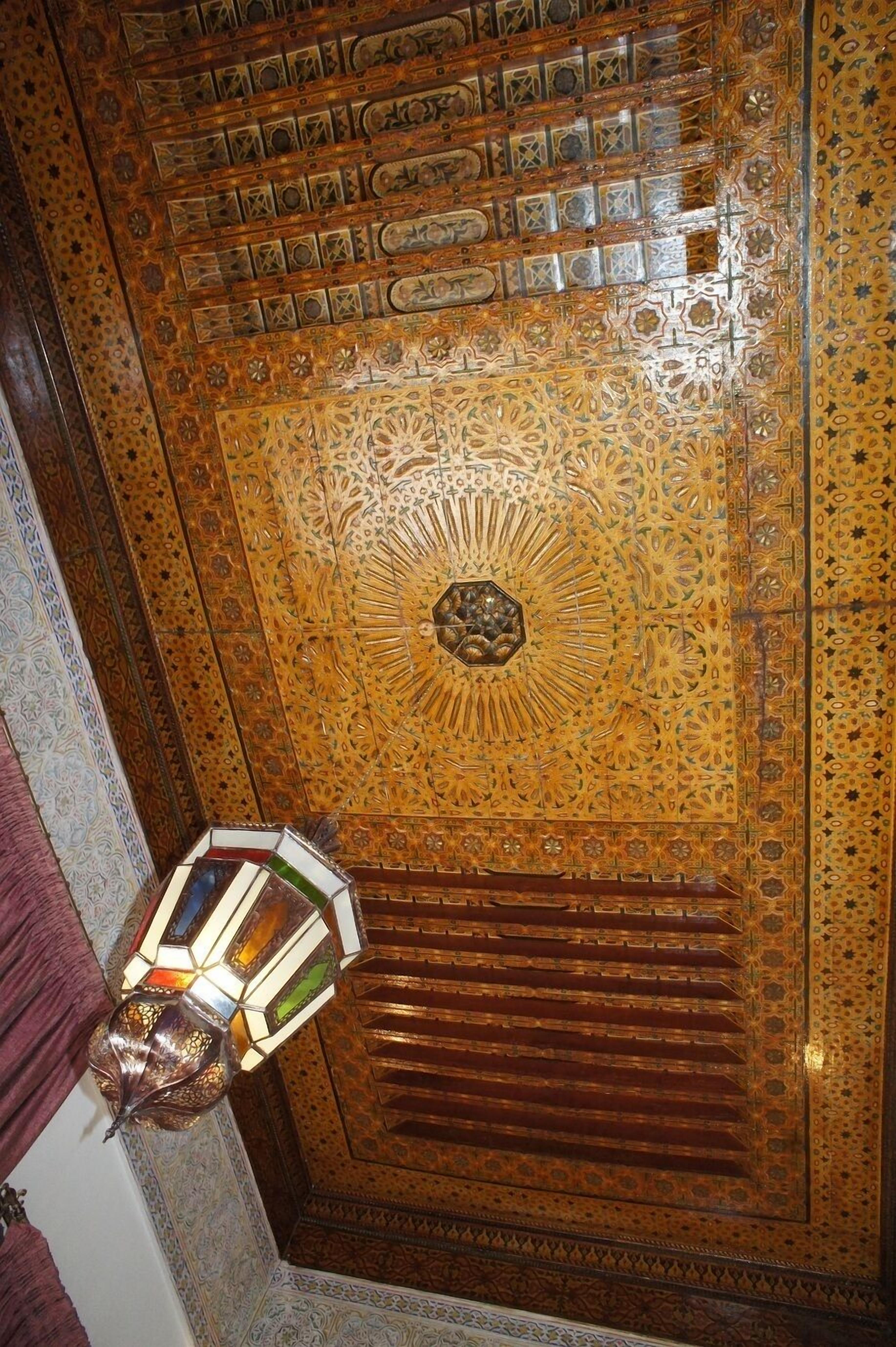 A richly decorated wooden door with intricate geometric and floral patterns, a hanging light fixture, and a patterned carpet.