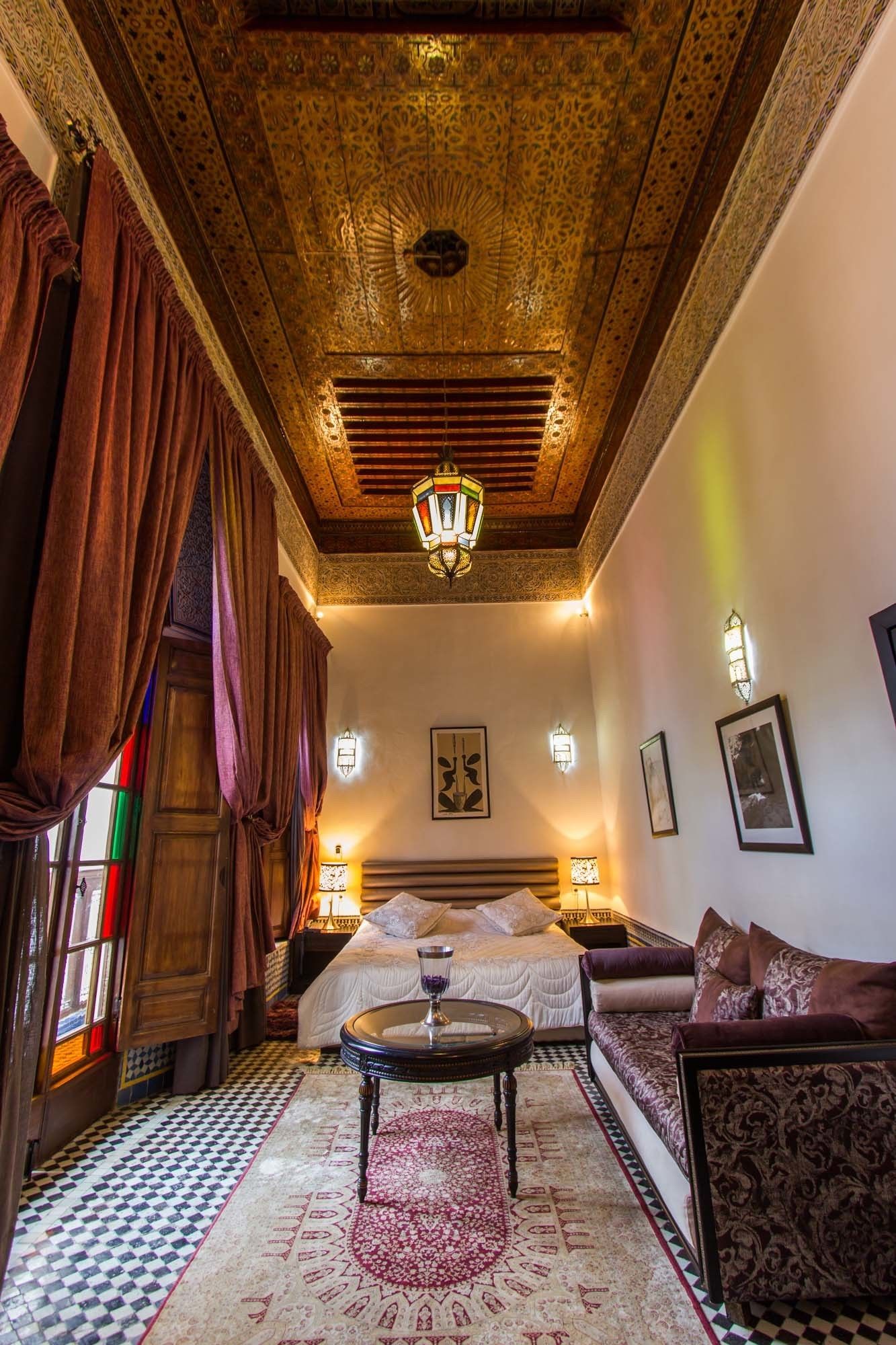A traditional room with a bed, a sofa, a chandelier, and patterned walls.