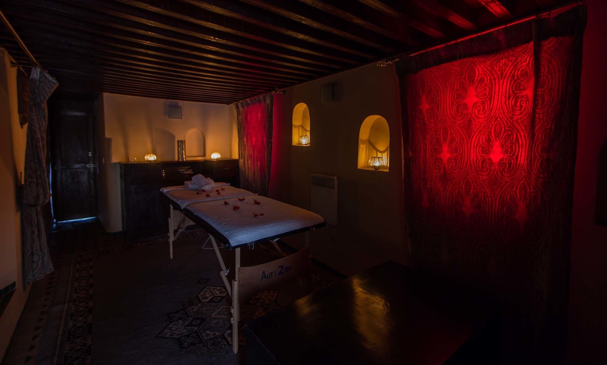 A dimly lit room with a massage table, a small cabinet, and a patterned red wall.