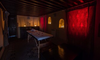 Una habitación poco iluminada con una camilla de masaje, un mueble bajo y una pared roja con diseño.