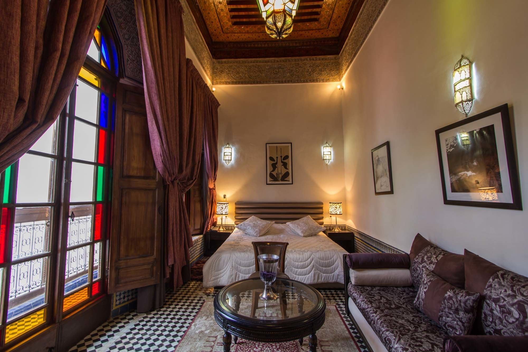 A hotel room with a large bed, a sofa, a glass table, and a chandelier.