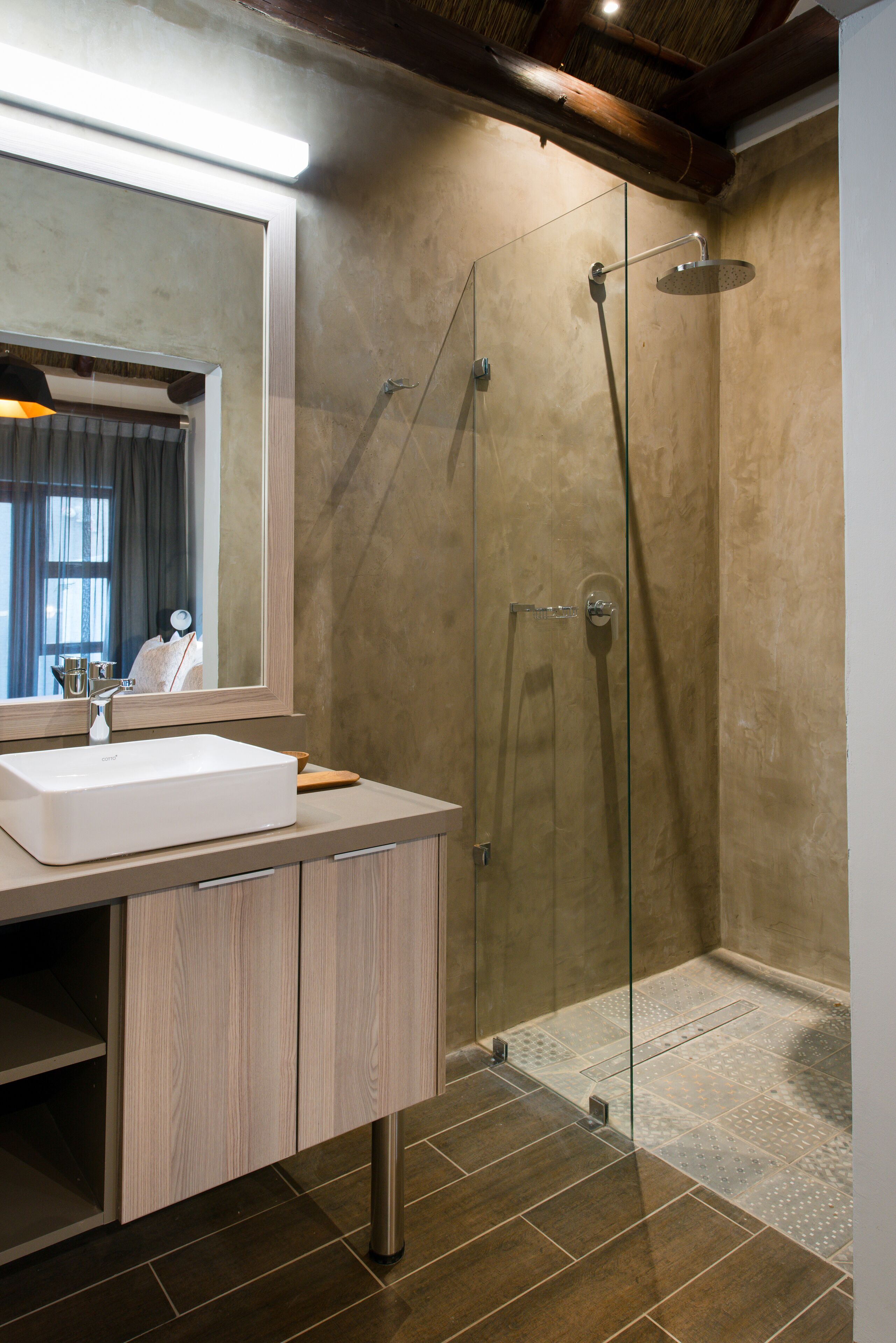 Een moderne badkamer met een grote spiegel, een wit wastafelmeubel, houten kastjes, een glazen douchecabine en een betegelde vloer.