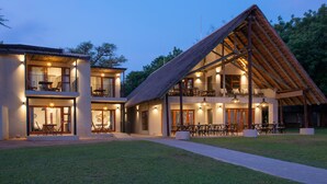 A modern two-story building with a thatched roof, outdoor seating, and a well-lit entrance.
