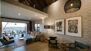 A spacious living area with a large window, a sofa, a coffee table, and a dining area with chairs and tables.