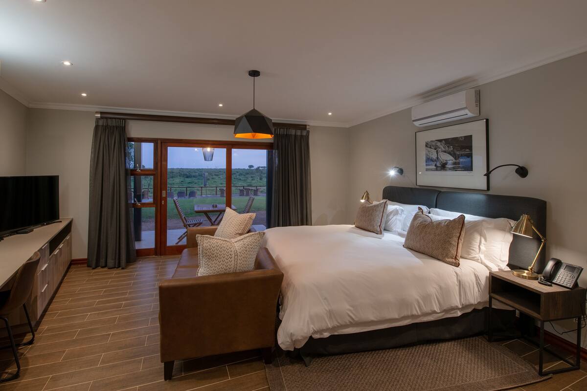 Une chambre d’hôtel moderne, dotée d’un grand lit, d’un bureau, d’une chaise et offrant une vue sur l’extérieur.