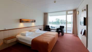 Ein Hotelzimmer mit einem Bett, zwei Sesseln, einem Fernseher und einem Fenster mit Blick auf ein Gewässer.