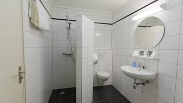 Un baño moderno con azulejos blancos, piso negro, ducha, inodoro y lavamanos con espejo.
