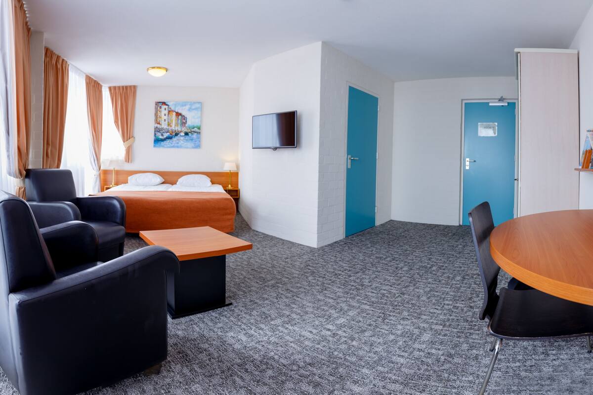 A hotel room with a bed, a TV, a desk, and a dining table.