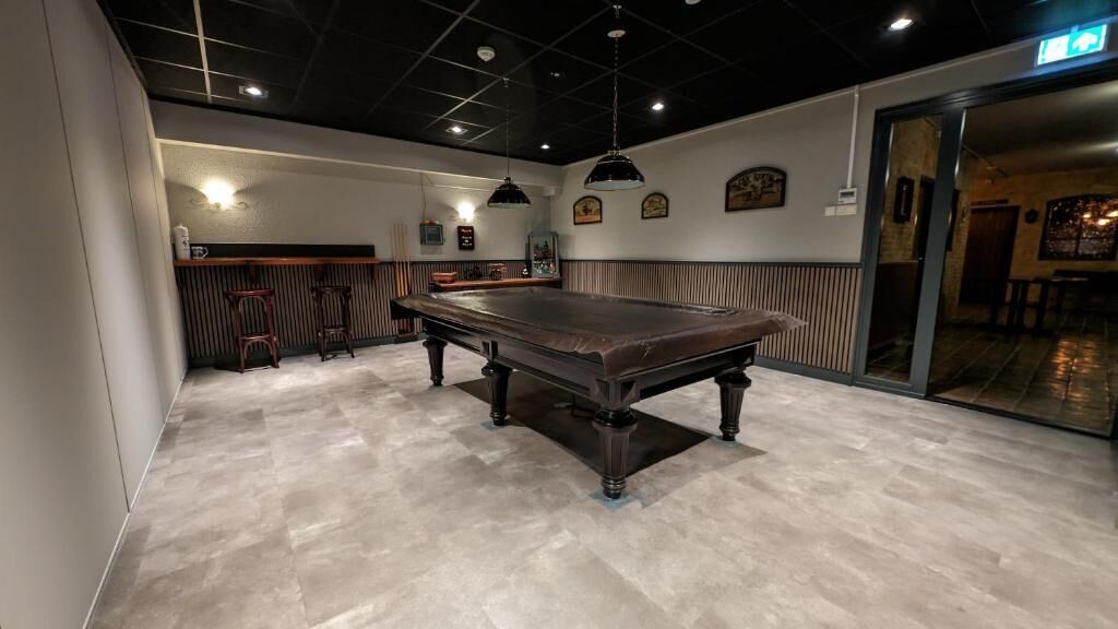 A billiards room with a pool table, cushioned seating, and pendant lighting.