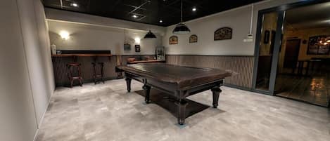 A billiards room with a pool table, cushioned seating, and pendant lighting.