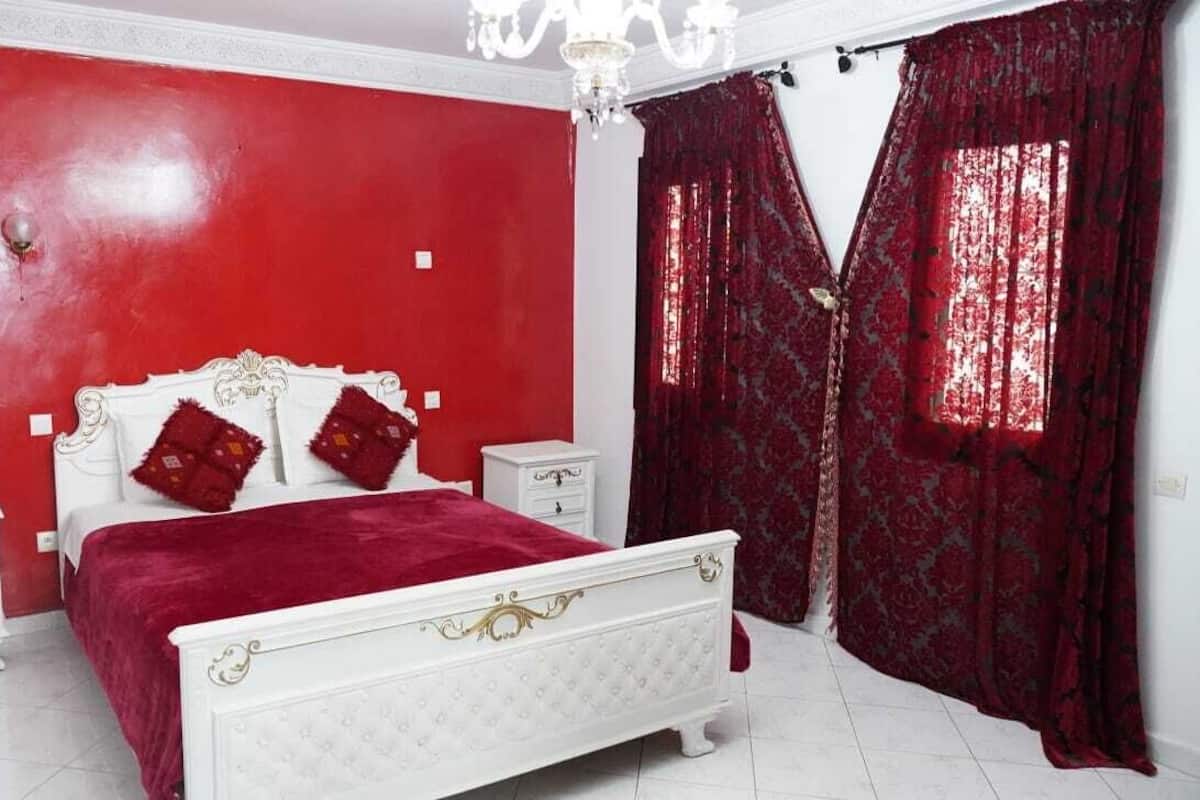 Un dormitorio con cama blanca, paredes rojas y una araña.
