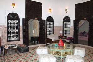 A traditional Moroccan interior with ornate doors, a patterned floor, and a central coffee table.