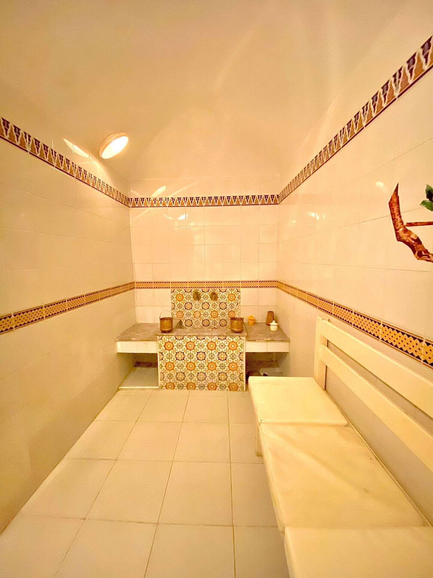 Ein kleines Badezimmer mit Fliesen, einer Bank, einem Waschbecken und einer dekorativen Wandverziierung.