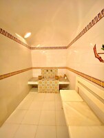 Un baño pequeño con azulejos, una banca, un lavamanos y un adorno en la pared.
