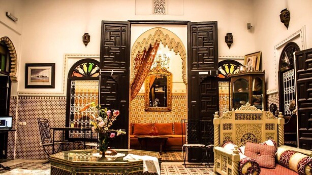 A traditional Moroccan interior with a central archway, ornate furniture, and a patterned floor. - Riad Baddi (Salé)