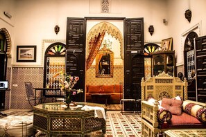 A traditional Moroccan interior with a central archway, ornate furniture, and a patterned floor.