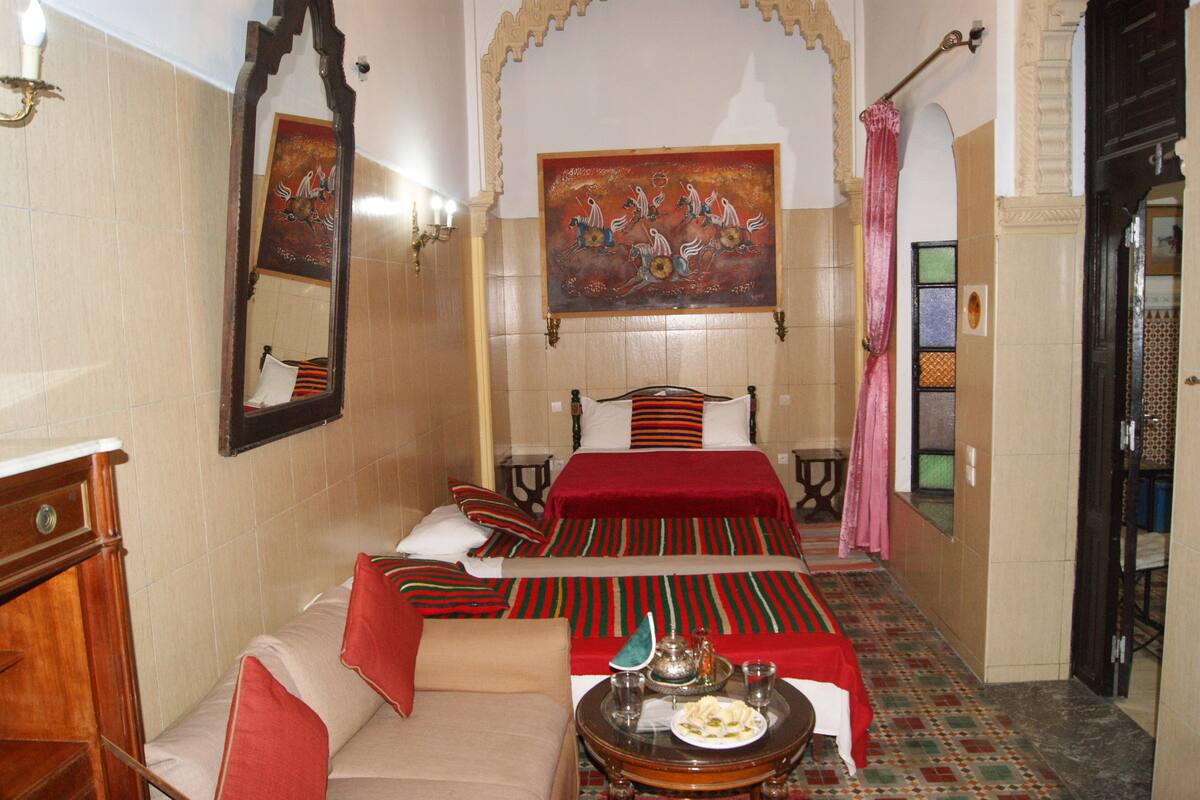 Habitación de hotel con una cama grande, una zona de estar, una mesa con una bandeja de comida y un cuadro en la pared.