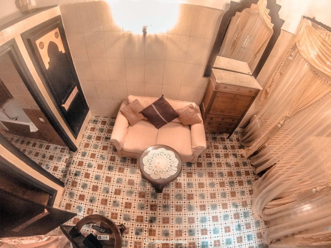 A bathroom with a patterned floor, a beige sofa, and a round table with a lace cover.