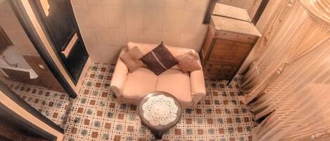 A bathroom with a patterned floor, a beige sofa, and a round table with a lace cover.