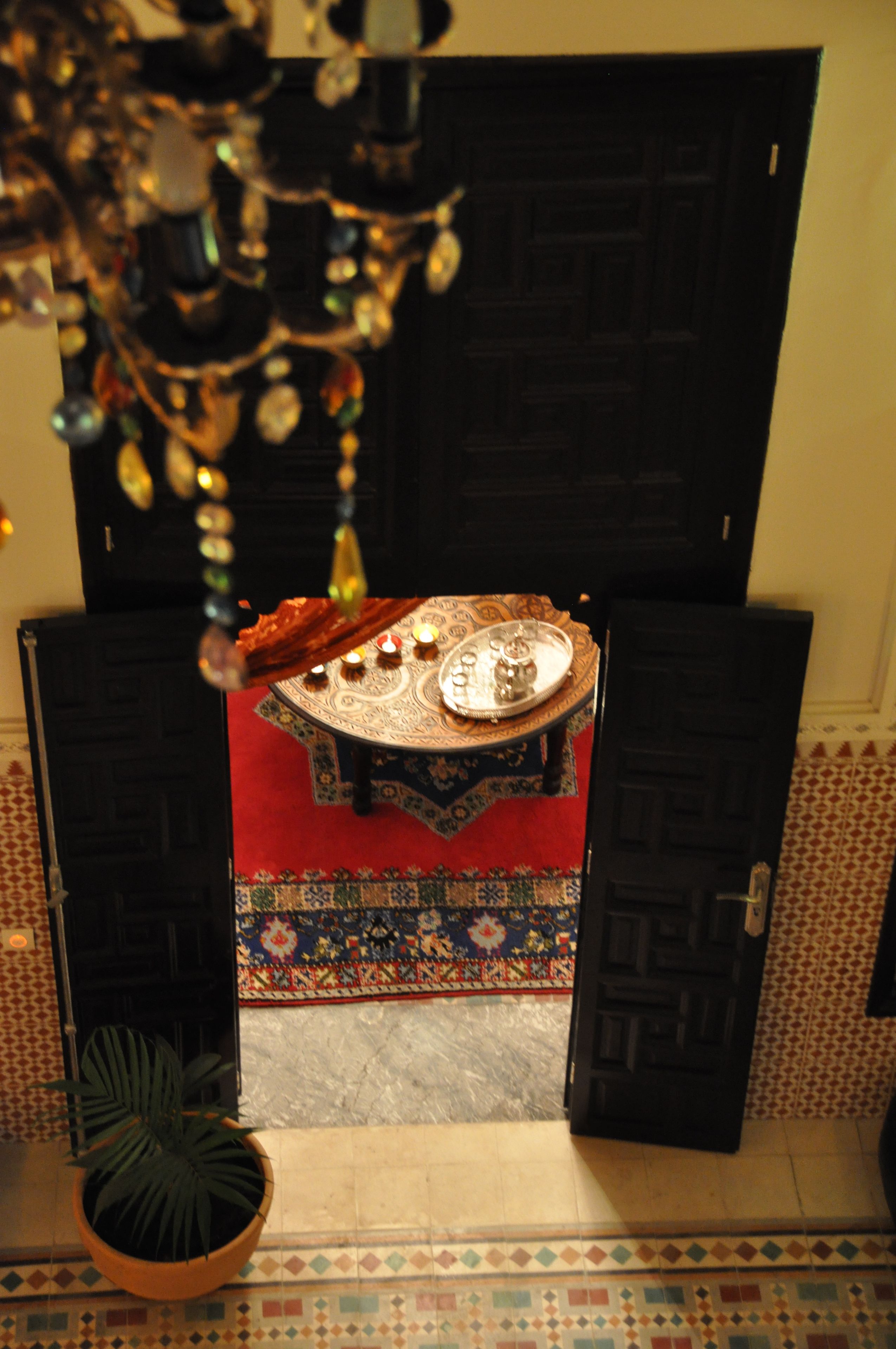 A room with a patterned carpet, a decorative table with a tray, and a potted plant.