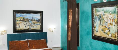 A bedroom with a bed, a sofa, a nightstand, and two wall-mounted paintings.