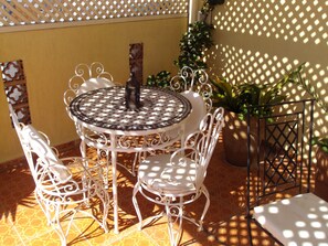 A round metal table with a patterned top, surrounded by white metal chairs with intricate designs.