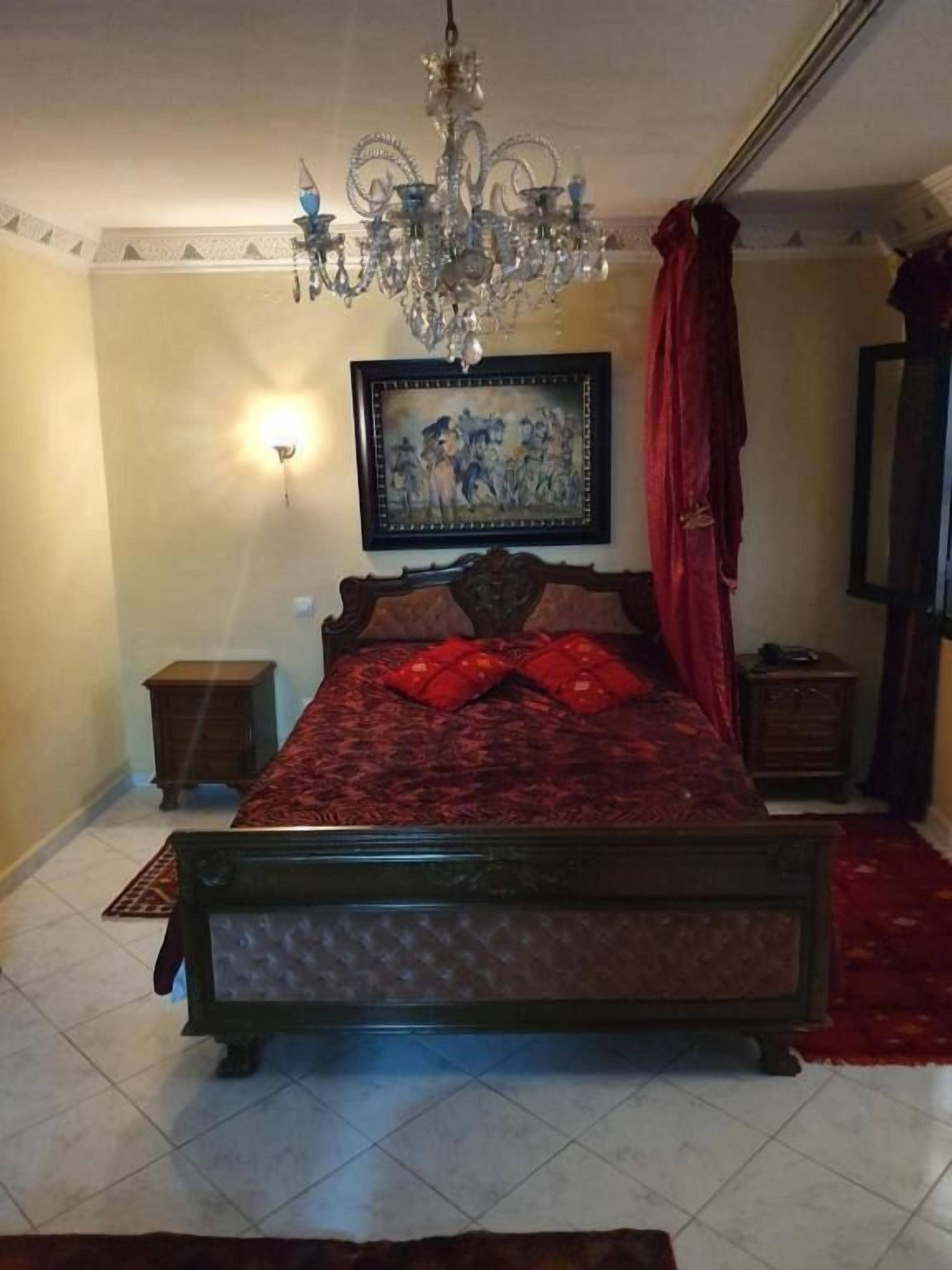 Un dormitorio con una cama grande, una araña, un cuadro en la pared y una cortina roja.