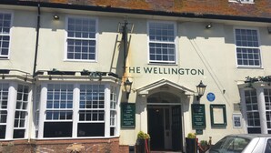 Un pub tradicional llamado "The Wellington" con una fachada clásica, ventanas amplias y mesas al aire libre.