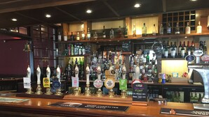 Un bar con varias griferías de cerveza, estanterías llenas de botellas y una pizarra con la carta.