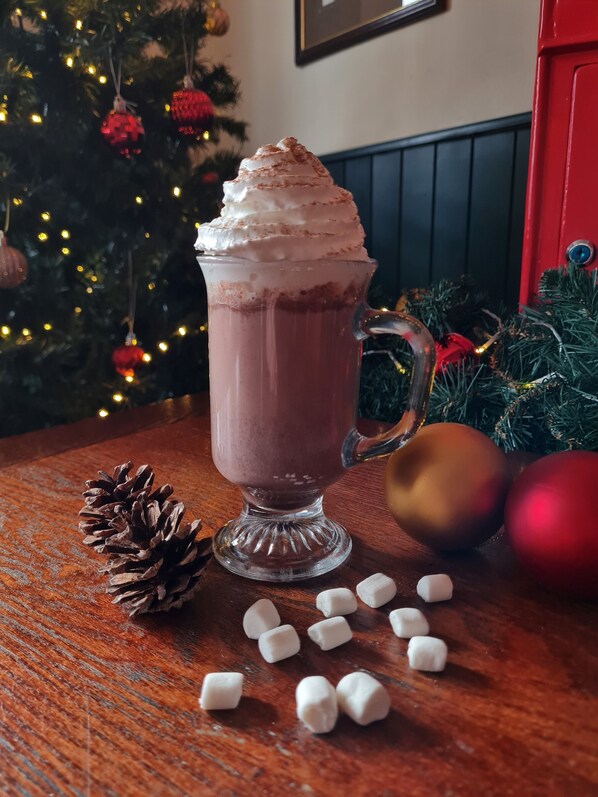 A glass mug with a handle filled with a frothy beverage, a pine cone, and marshmallows on a wooden surface.