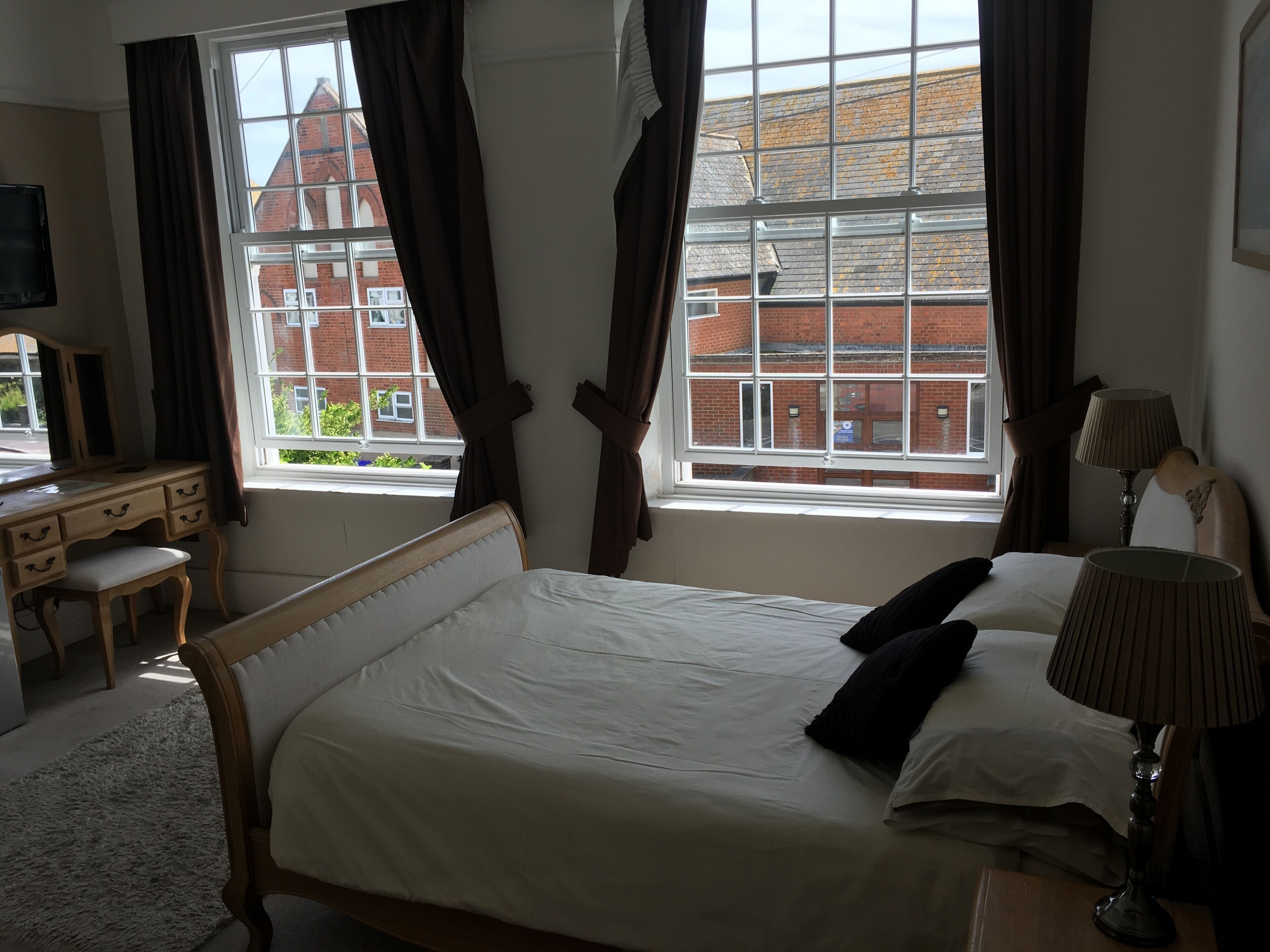 Un dormitorio con cama, escritorio, silla y ventana con cortinas.